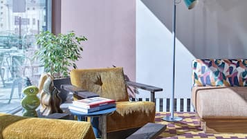 Una sala moderna con un sofá, un sillón y una lámpara de pie. Hay una planta y una mesita con libros.