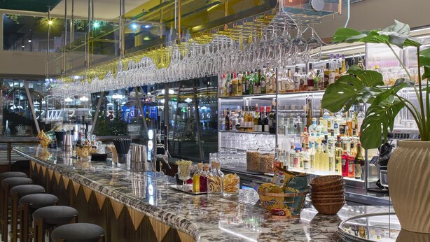 A bar area with a long counter, multiple glasses hanging above, and a variety of bottles and snacks on the counter. - Scandic Malmen (Stockholm)