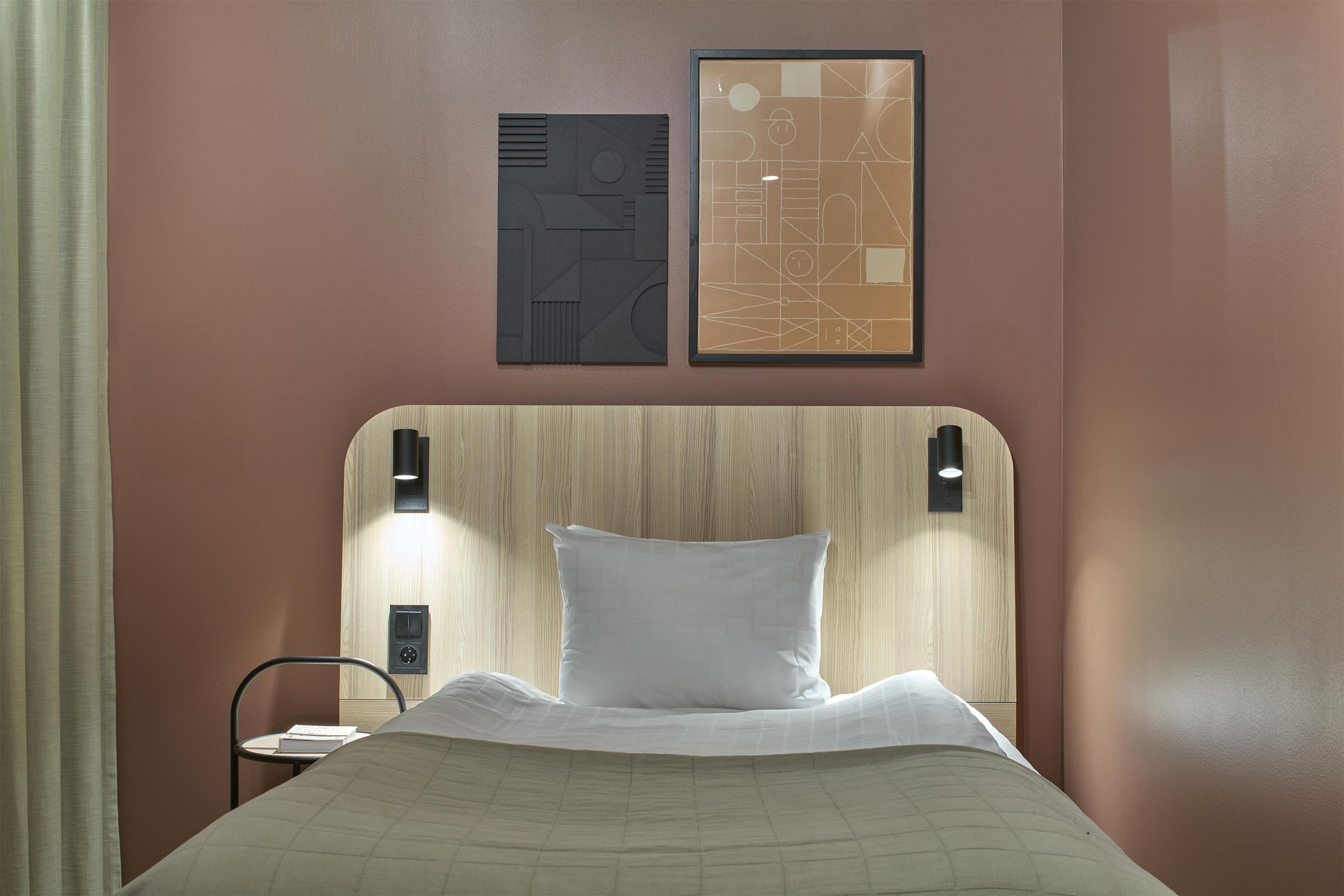 A hotel room with a wooden headboard, a white pillow, and two framed artworks on the wall.