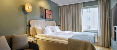 Une chambre d’hôtel avec un lit, un canapé, une table de chevet, une lampe et une fenêtre avec des rideaux.