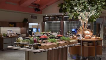 Een buffetgedeelte met diverse gerechten, waaronder fruit, groenten en vlees, in een goed verlichte ruimte met houten meubels en een grote plant.