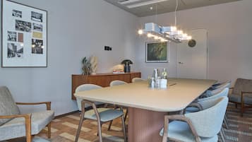 A modern meeting room with a large table, chairs, a wooden cabinet, and a framed collage on the wall.