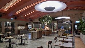 A spacious restaurant with high ceilings, pendant lighting, and a central tree. - Scandic Malmen (Stockholm)