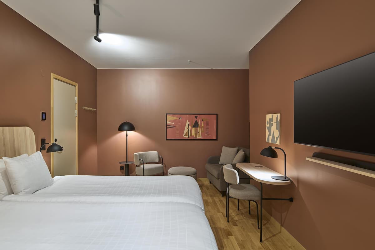 Ein Hotelzimmer mit einem großen Bett, einem Schreibtisch, einem Sessel, einem Fernseher und Bildern an den Wänden.