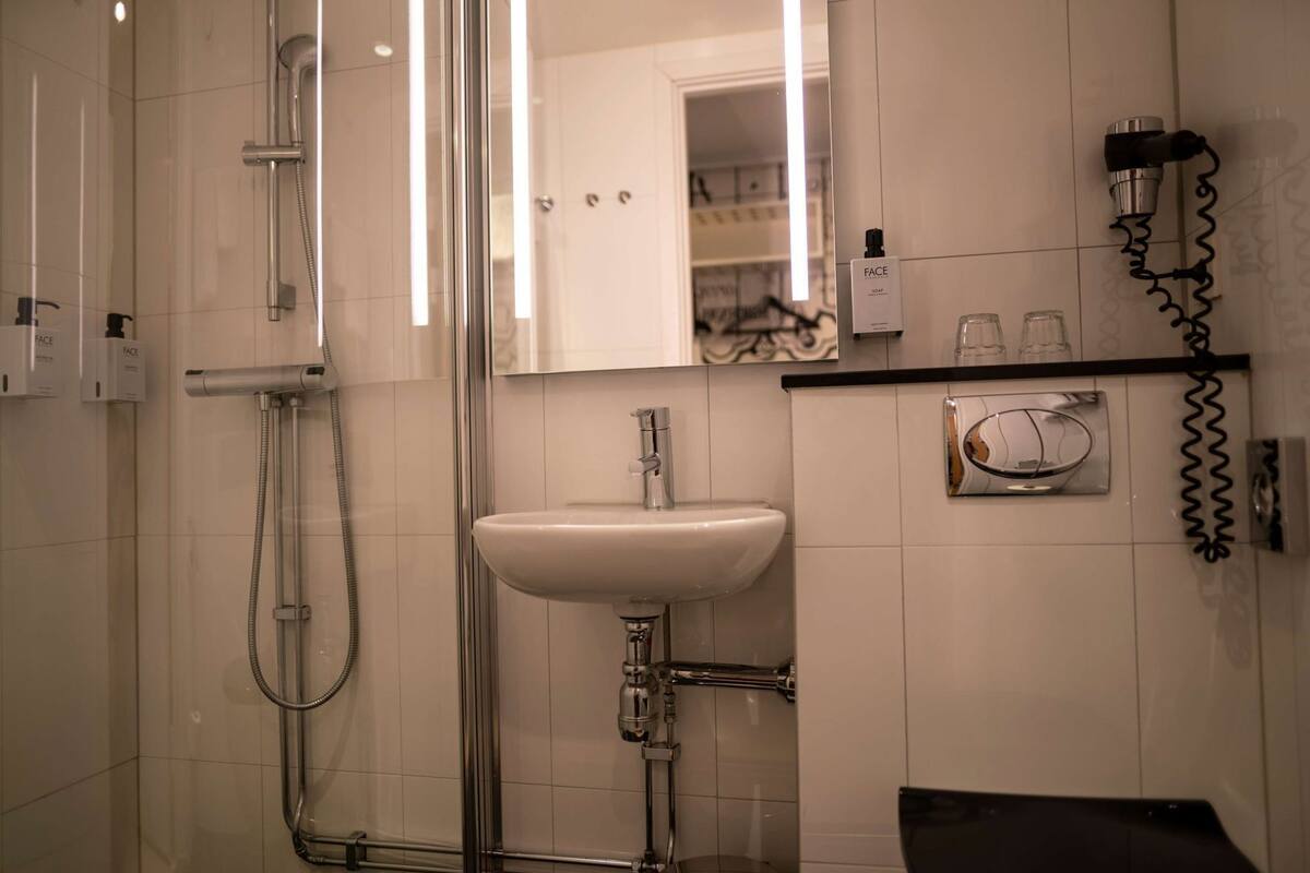 Ein modernes Badezimmer mit einer Duschkabine aus Glas, einem weißen Waschbecken und einem Spiegel darüber.