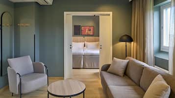 A hotel room with a sofa, armchair, round table, and a bed with a headboard.