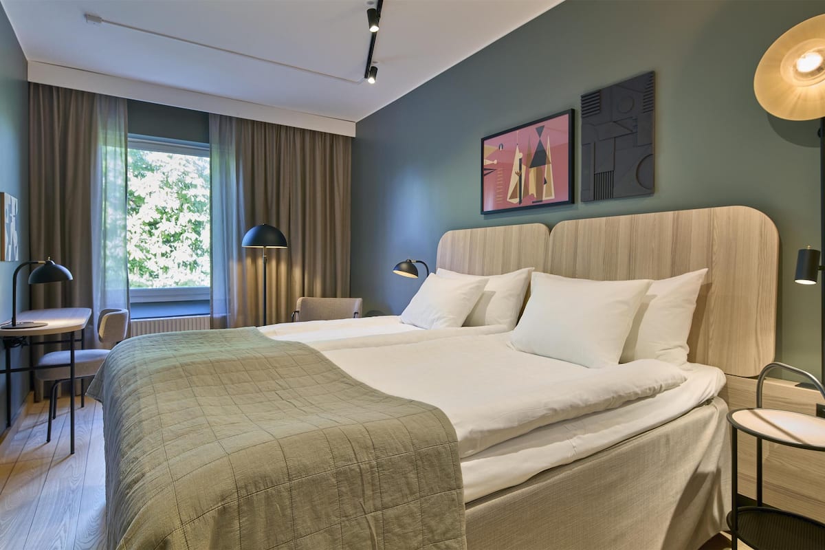 Ein Hotelzimmer mit einem großen Bett, zwei Nachttischen, einem Schreibtisch mit Stuhl und einem Fenster mit Vorhängen.