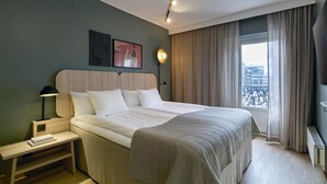 A modern hotel room with a large bed, a bedside table, a lamp, and a view of the city through the window. - Scandic Malmen (Stockholm)