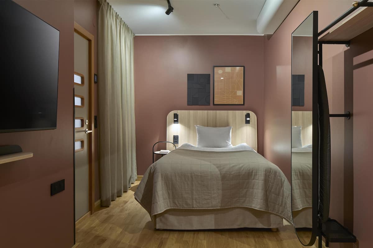 Ein modernes Hotelzimmer mit einem großen Bett, einem Flachbildfernseher, einem Nachttisch und einem Spiegel.