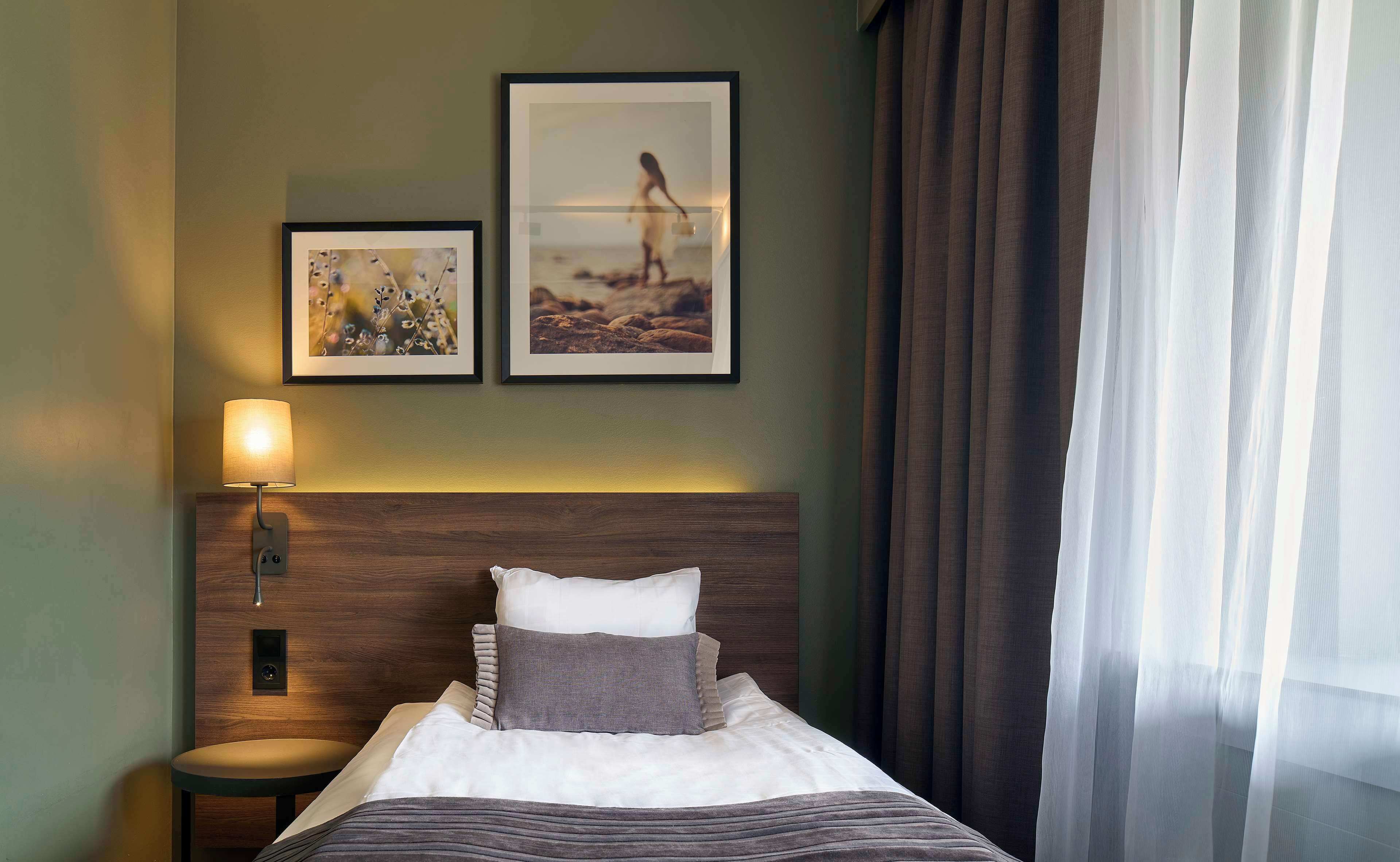 A neatly made bed with pillows and a headboard, a bedside table with a lamp, and two framed pictures on the wall.