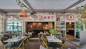 A restaurant interior with tables and chairs, a sign reading "RUBY", and a bar area. - Scandic Rubinen (Gothenburg)