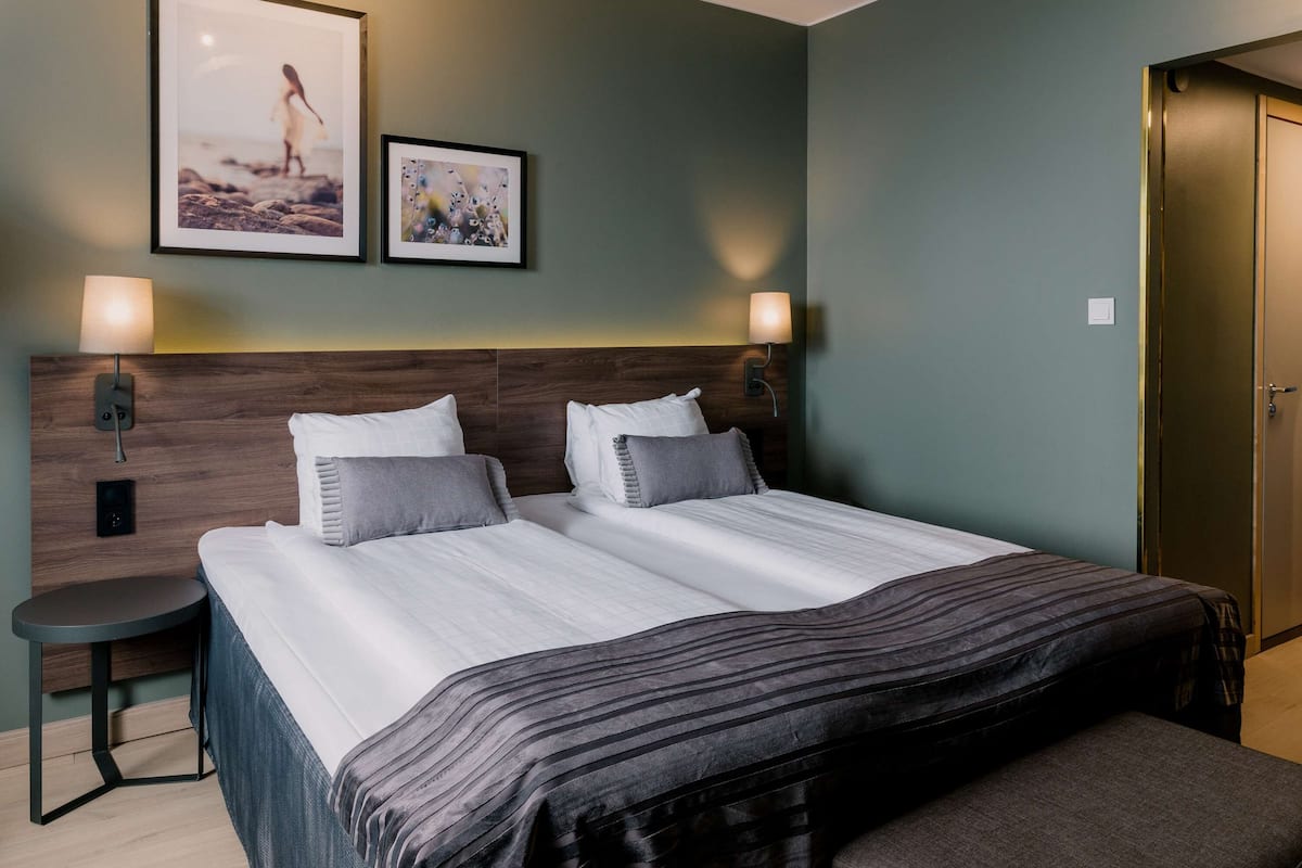 A double bed with a wooden headboard, two bedside tables with lamps, and two framed pictures on the wall.