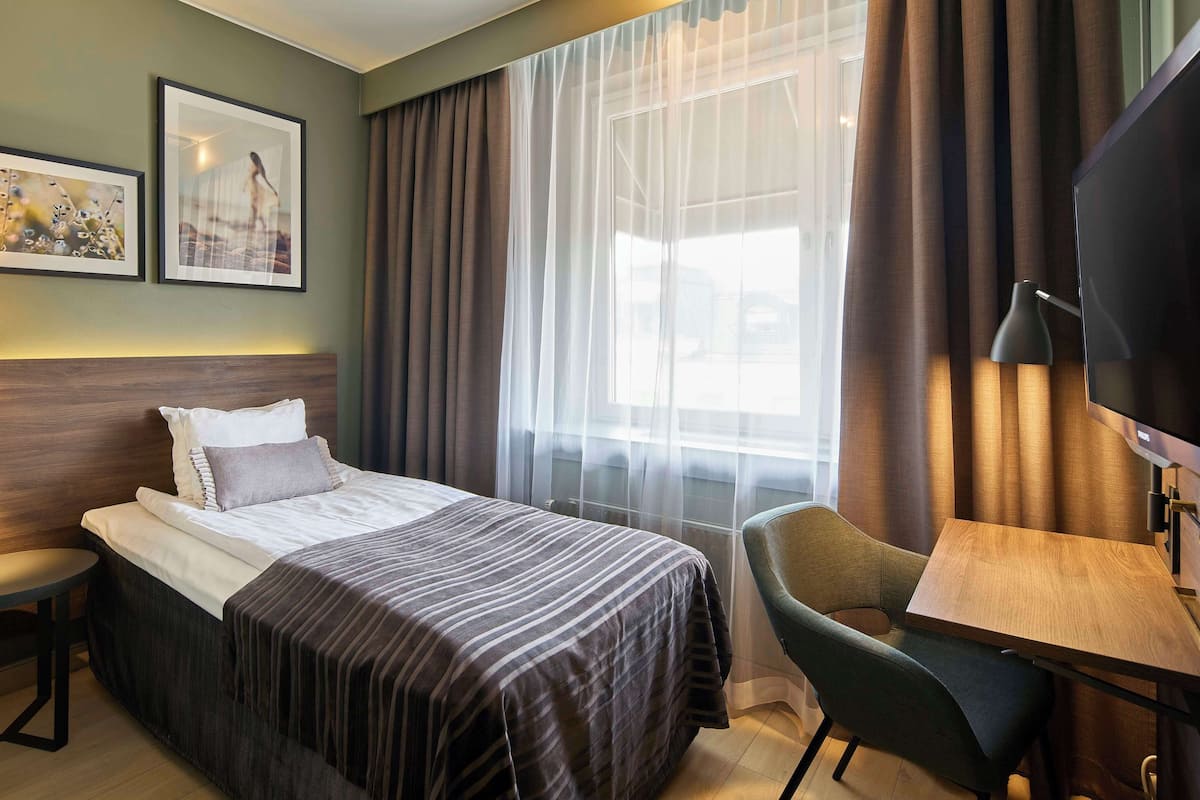 A hotel room with a bed, a desk, a chair, a TV, and two framed pictures on the wall.