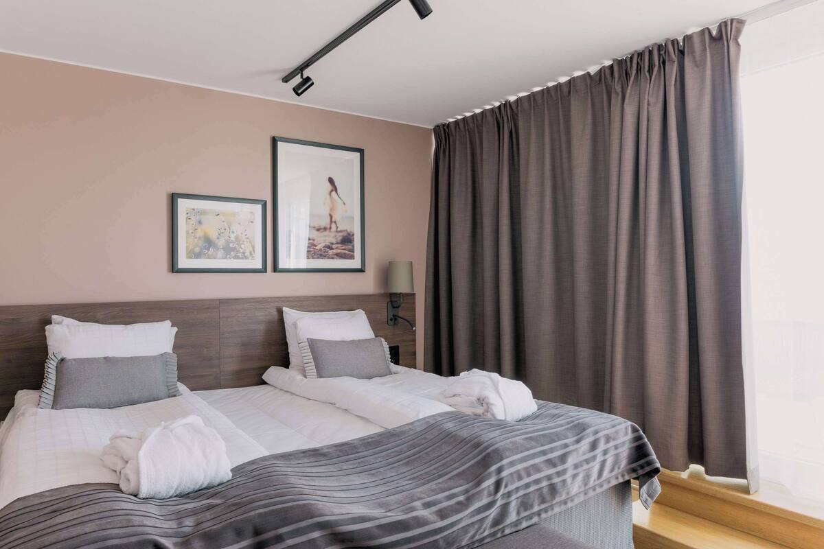 A hotel room with a bed, two framed pictures on the wall, a bedside lamp, and a window with curtains.