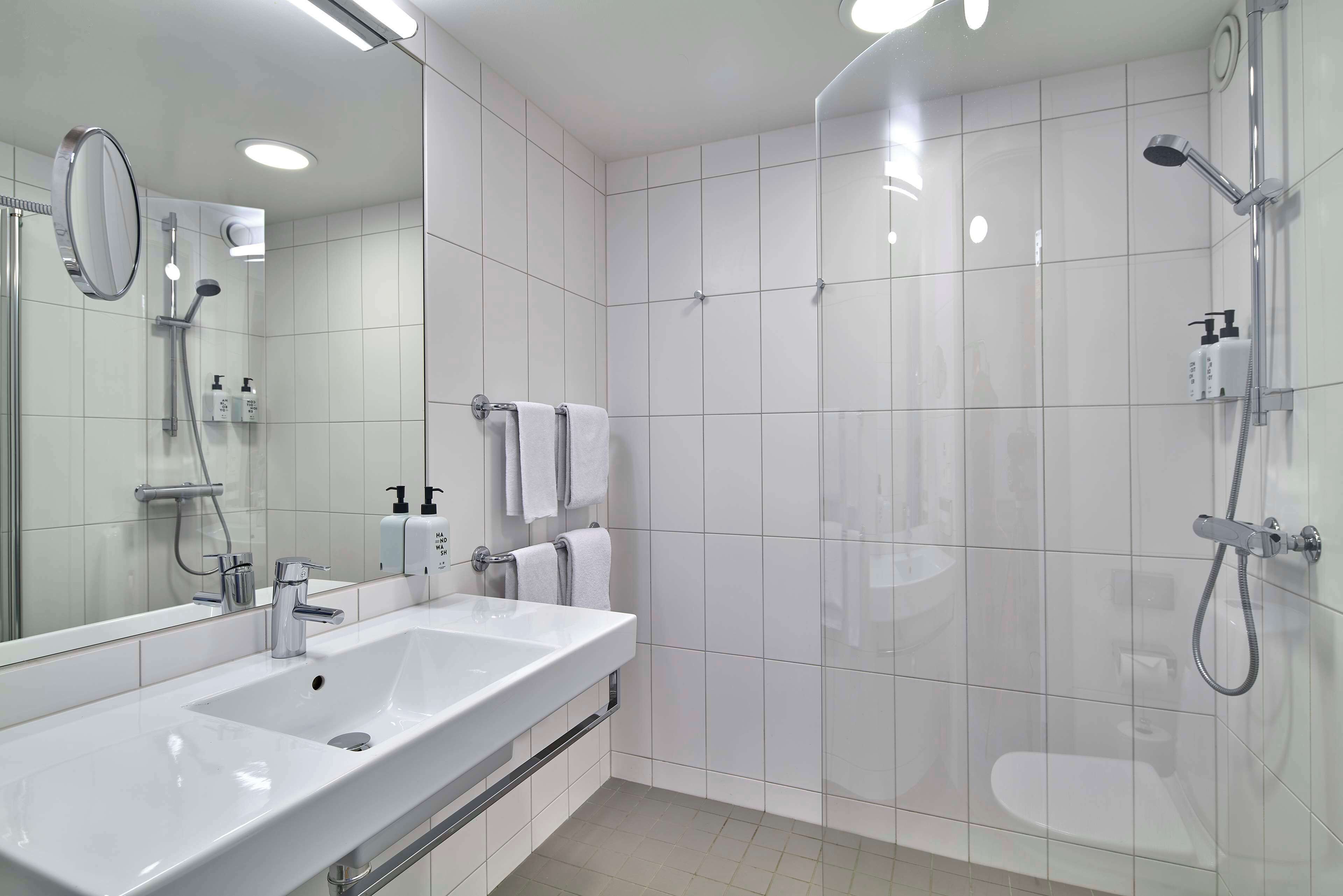 Un baño moderno con un espejo grande, lavamanos doble, ducha e inodoro.
