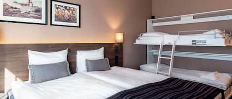 Habitación de hotel con literas, una cama grande con almohadas, una mesita de noche y cuadros enmarcados en la pared.