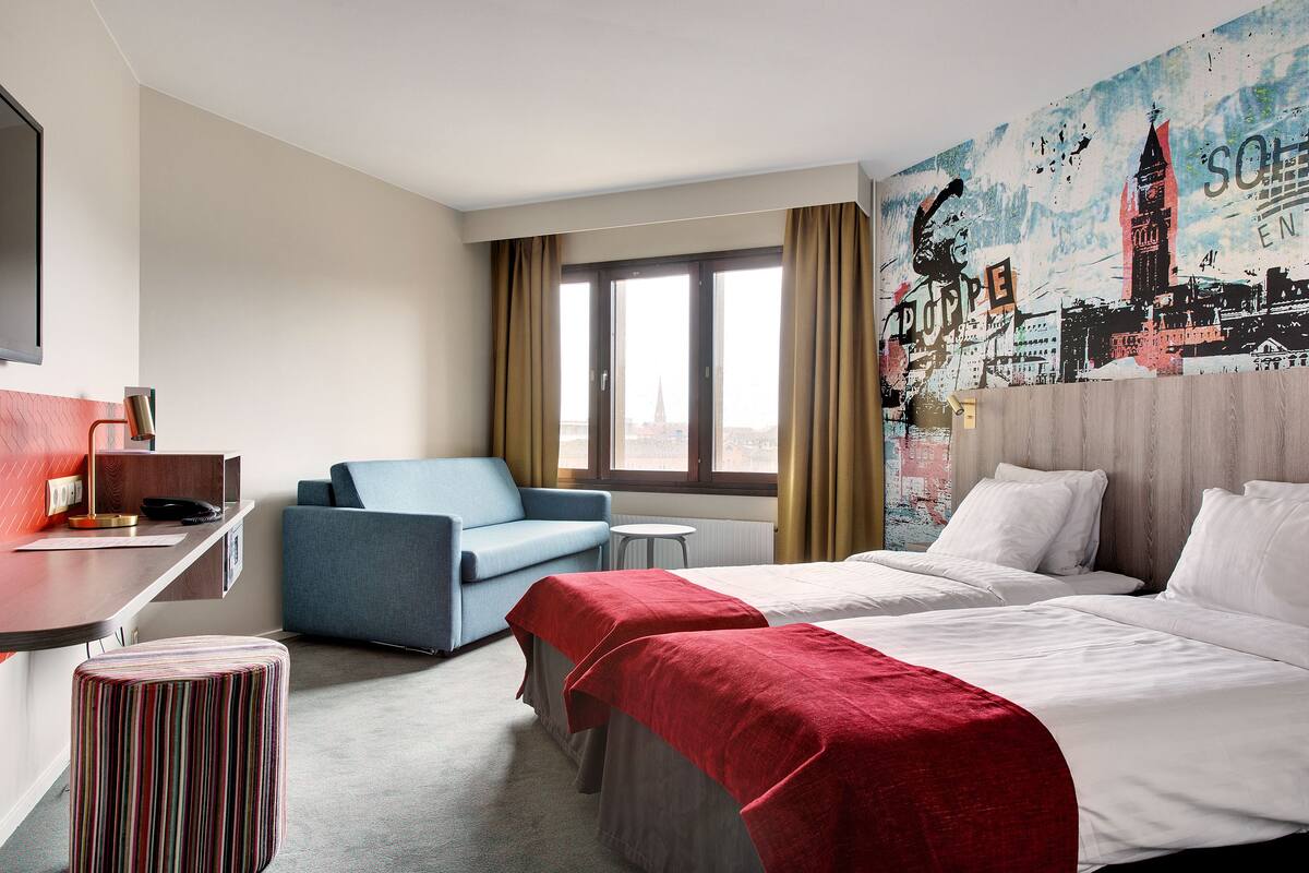 A hotel room with a bed, a desk, a chair, and a window with curtains.