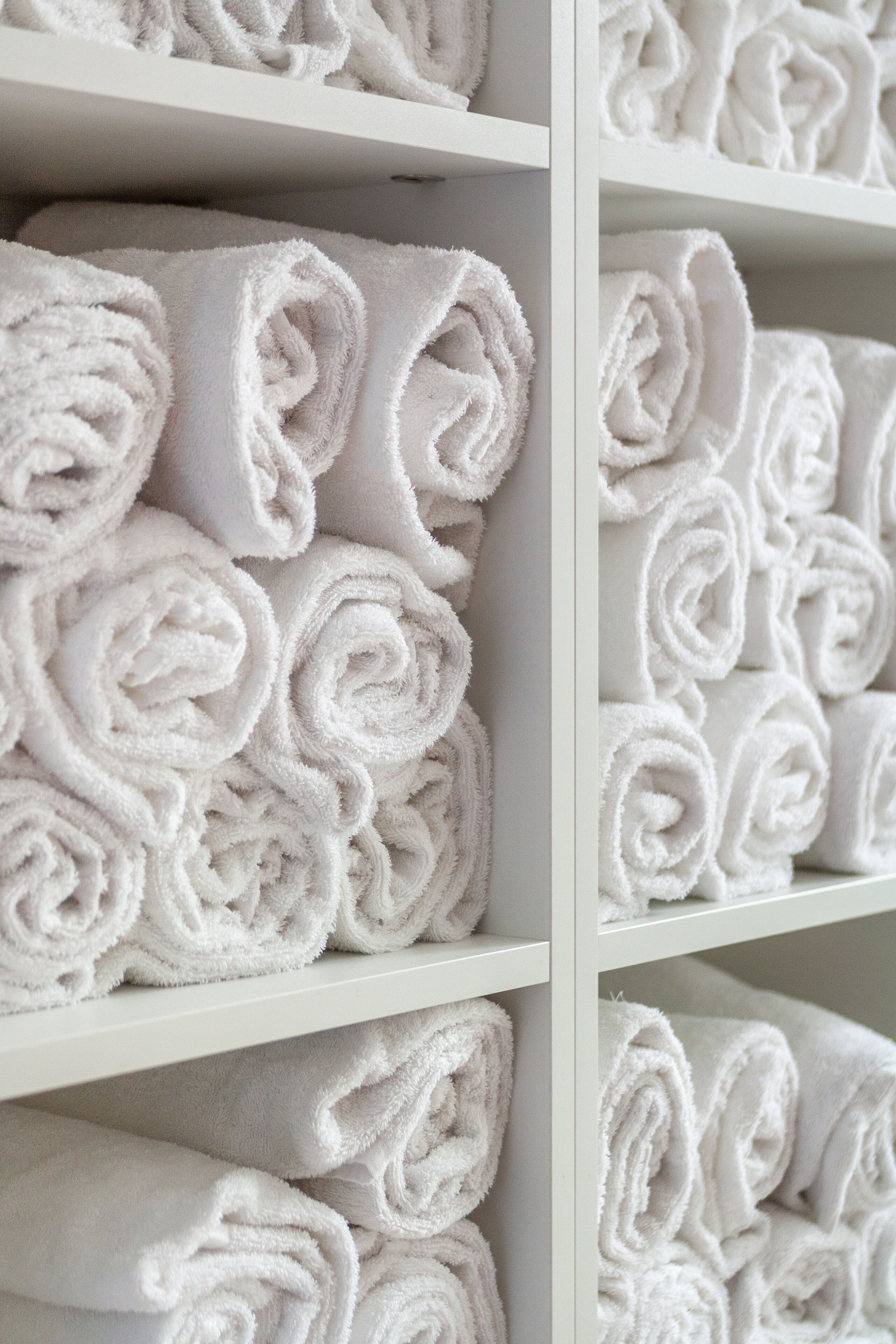 Neatly stacked white towels on white shelves.