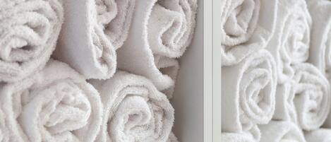 Neatly stacked white towels on white shelves.