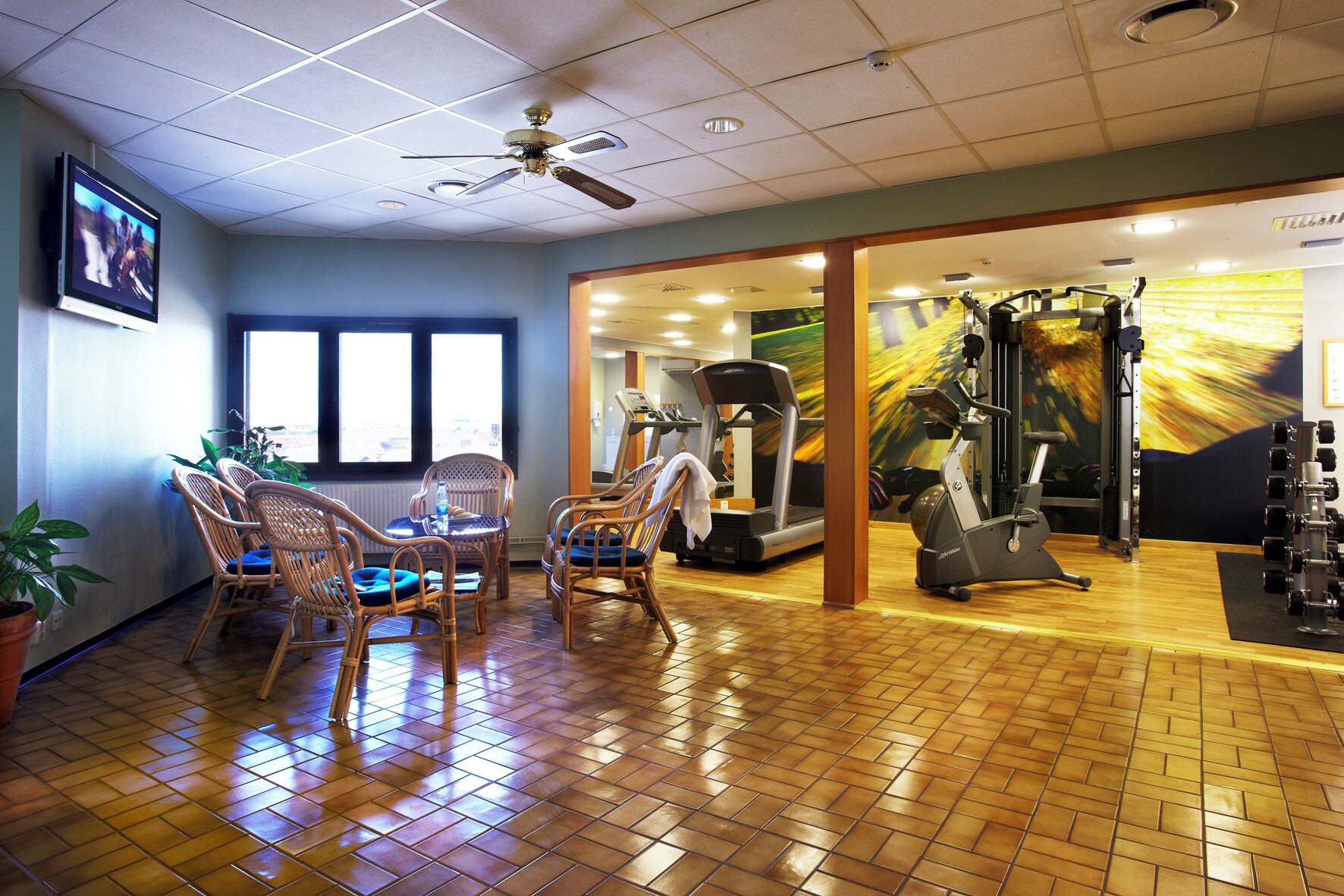 A gym with exercise equipment, wicker chairs, and a ceiling fan.