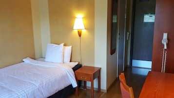 Quarto de hotel com cama, mesa de cabeceira, luminária e uma cadeira de madeira.