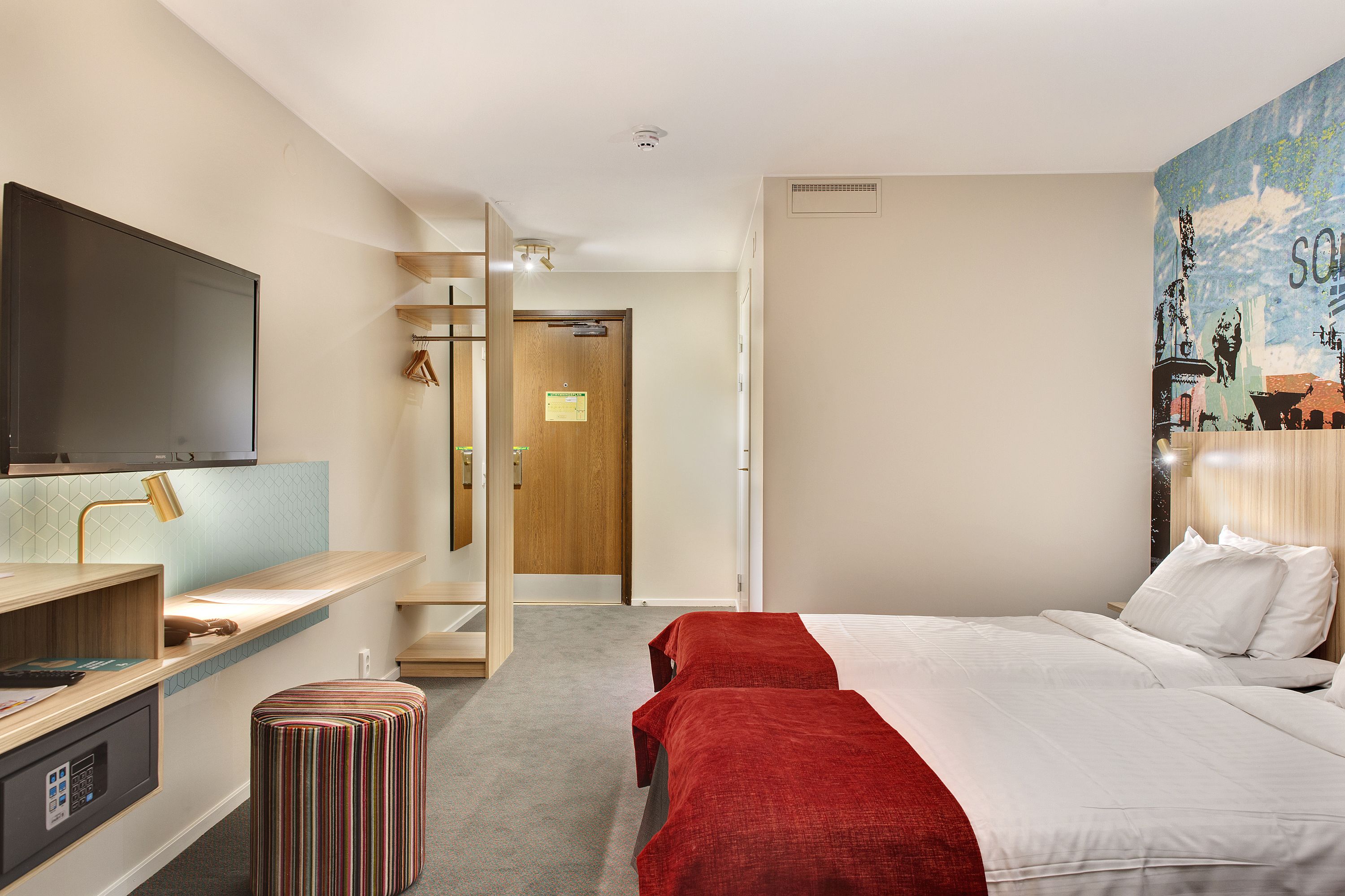 A hotel room with a bed, a desk with a computer, a TV, and a bathroom with a shower.