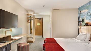 A hotel room with a bed, a desk with a computer, a TV, and a bathroom with a shower.