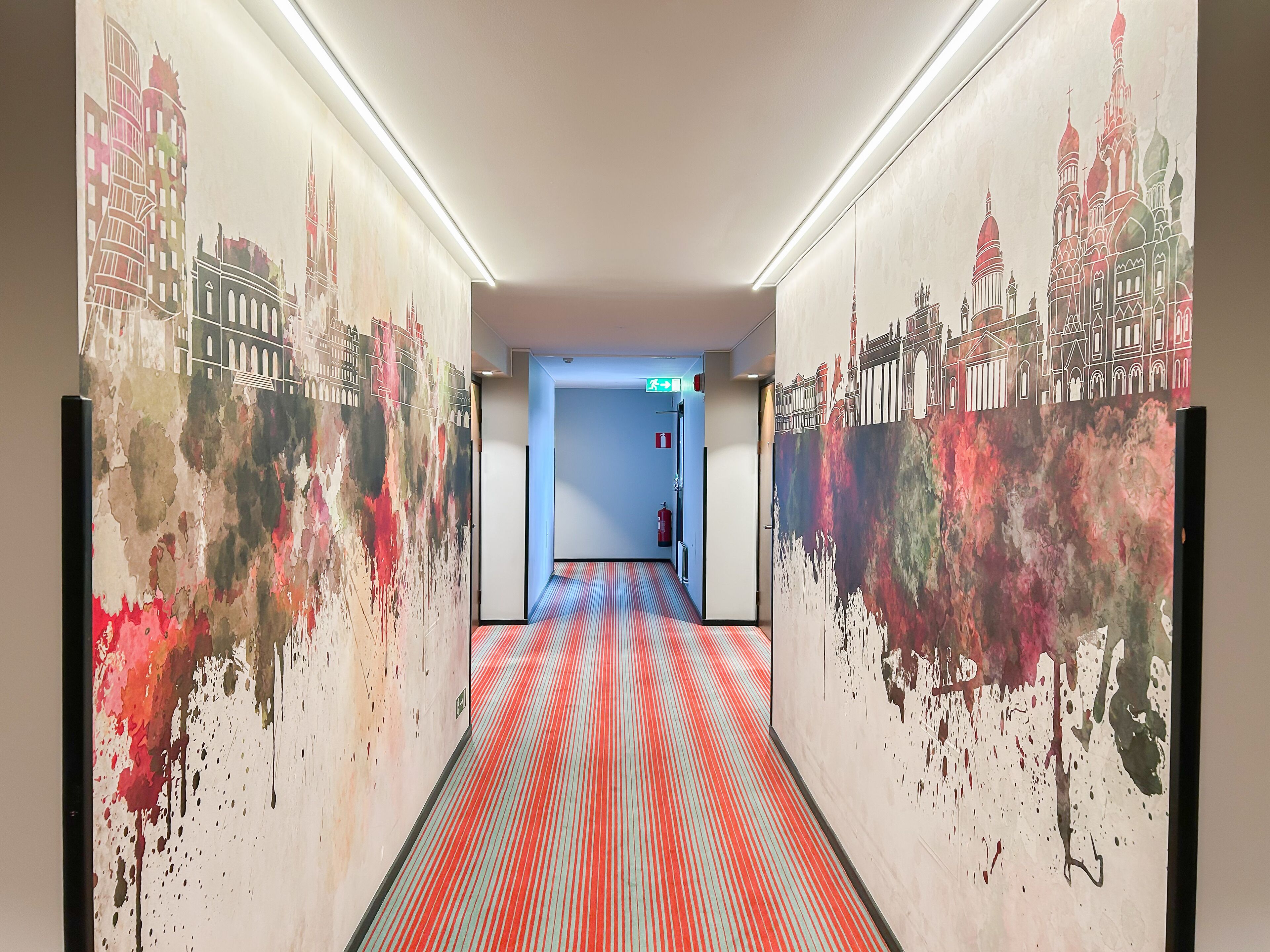 En hall med ett rött och blått randigt golv, väggar dekorerade med väggmålningar som föreställer stadsvyer, och en blå dörr längst ner.