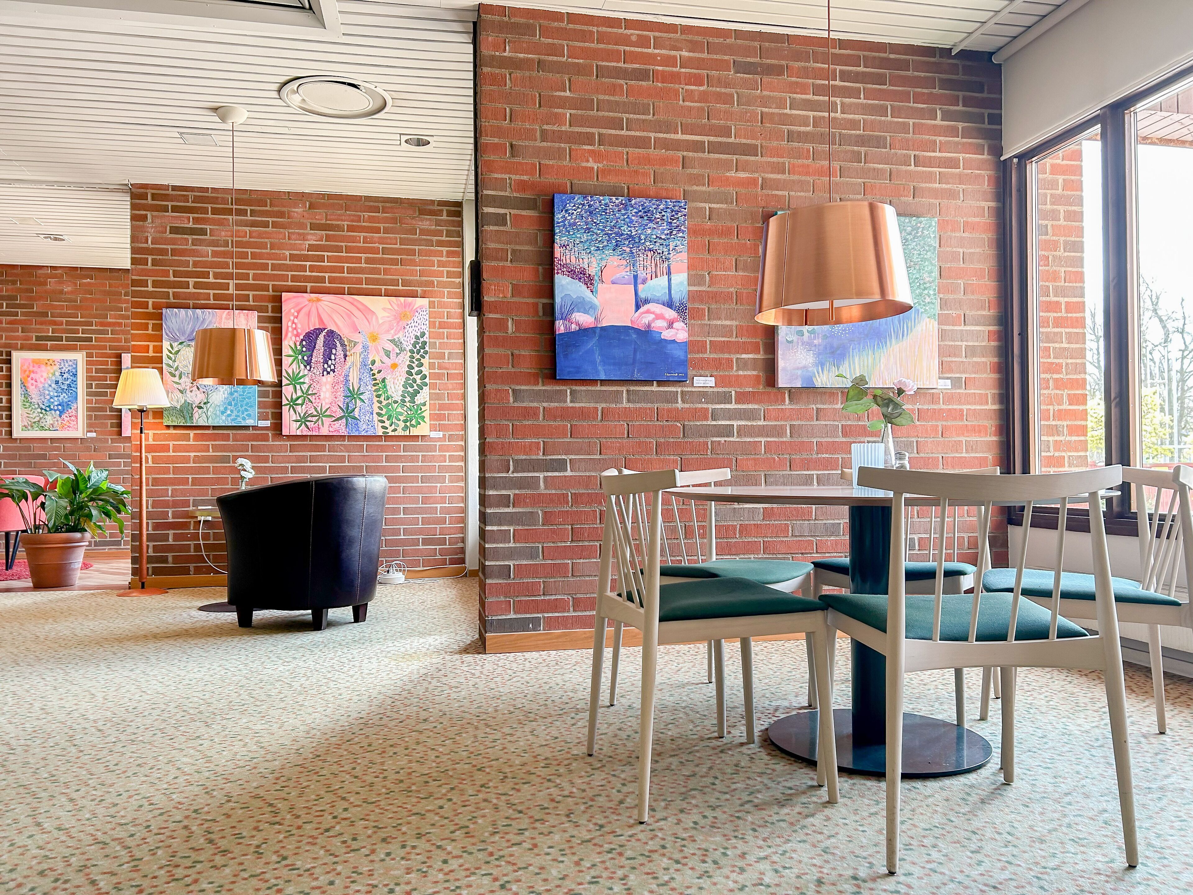 A room with a brick wall, a round table with chairs, and several paintings.
