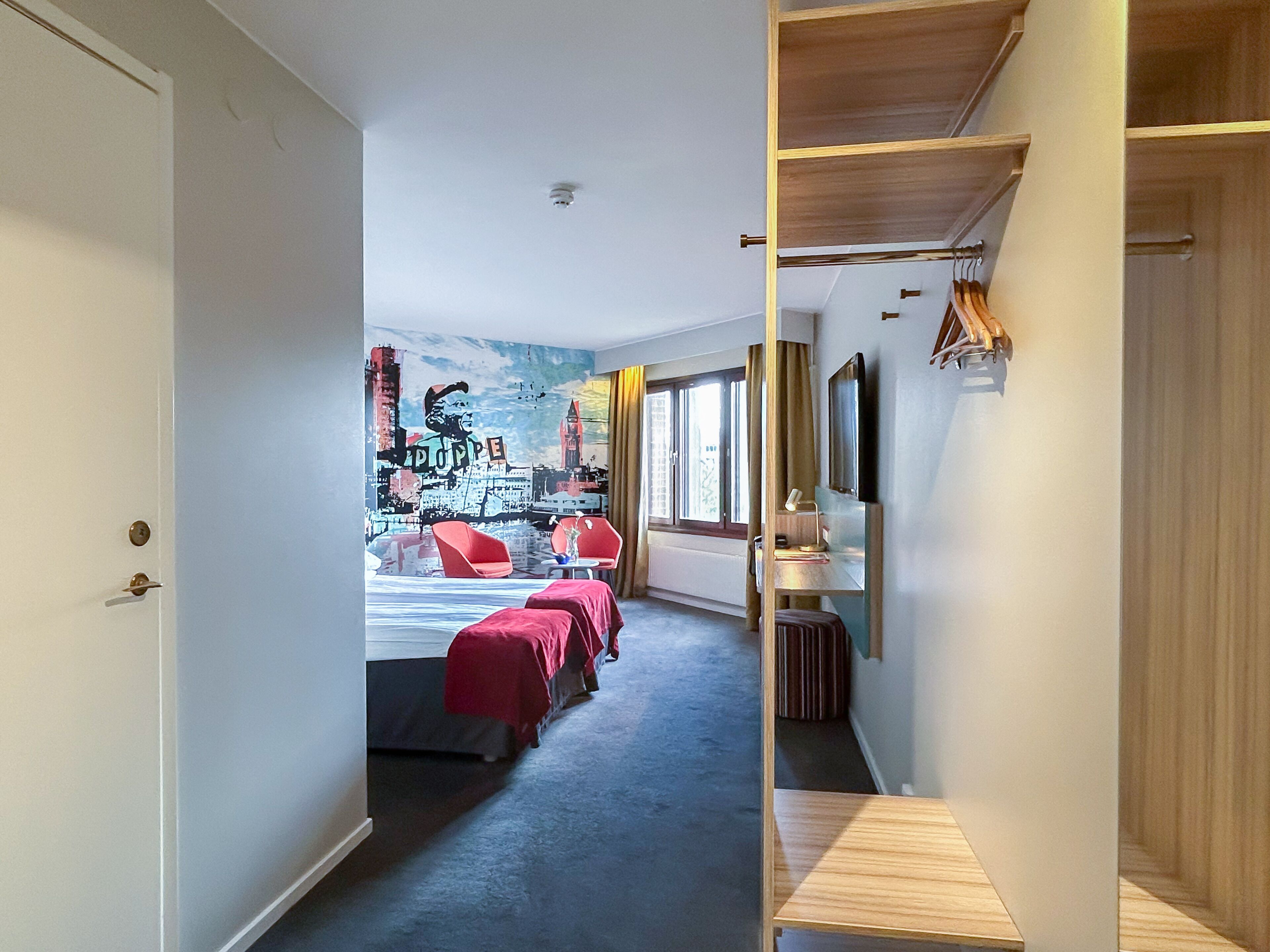 Habitación de hotel con cama, escritorio y silla. Ventana con cortinas y vista a la ciudad.