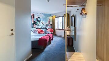 Habitación de hotel con cama, escritorio y silla. Ventana con cortinas y vista a la ciudad.