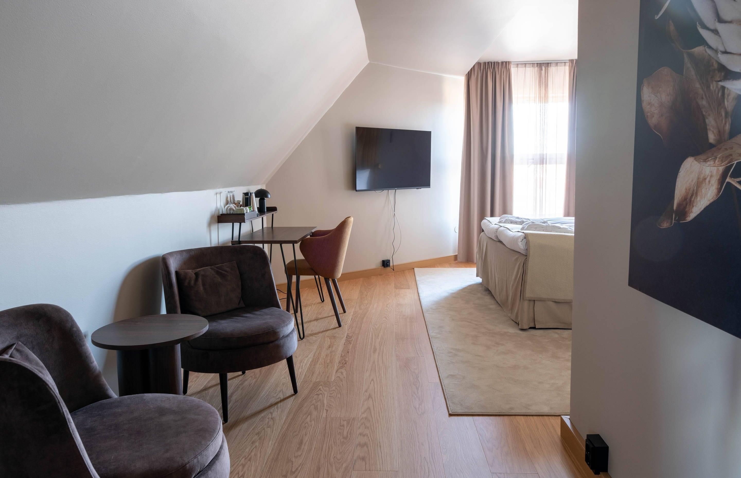 Una habitación moderna y luminosa con televisión de pantalla plana en la pared, un sofá, una mesita y una cama con vistas al exterior.
