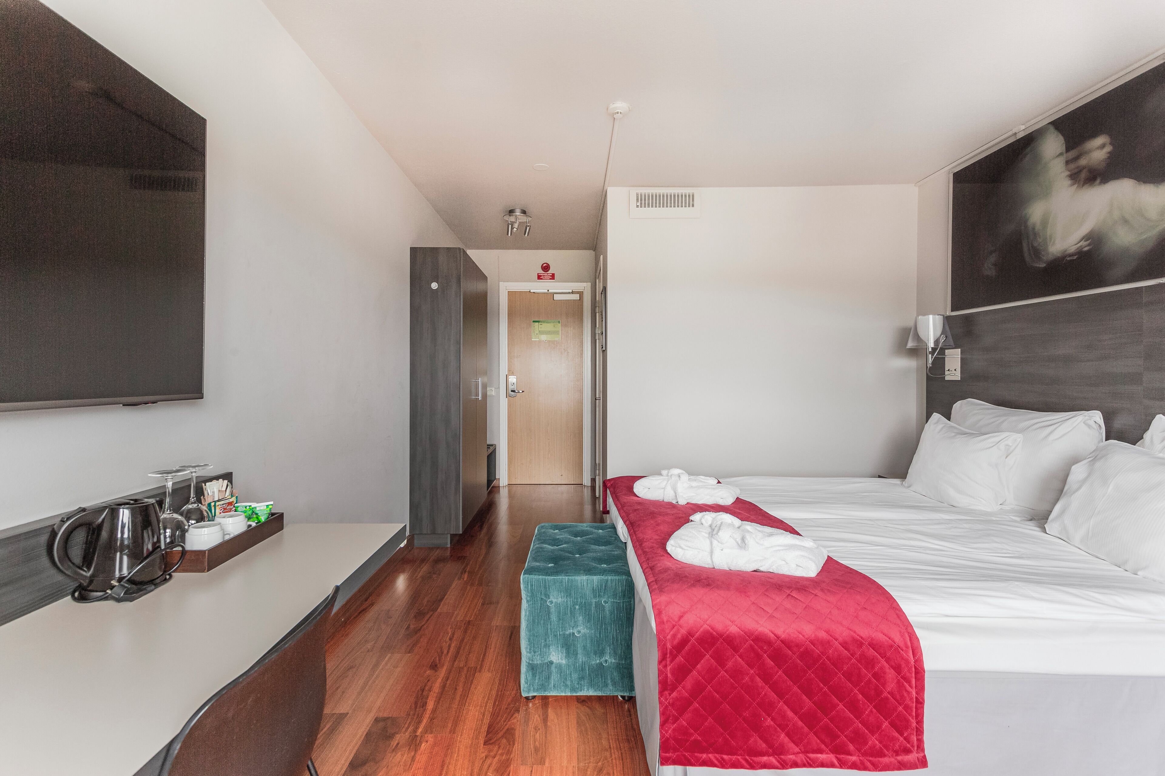A hotel room with a bed, a TV mounted on the wall, a coffee station, and a door leading to another room.