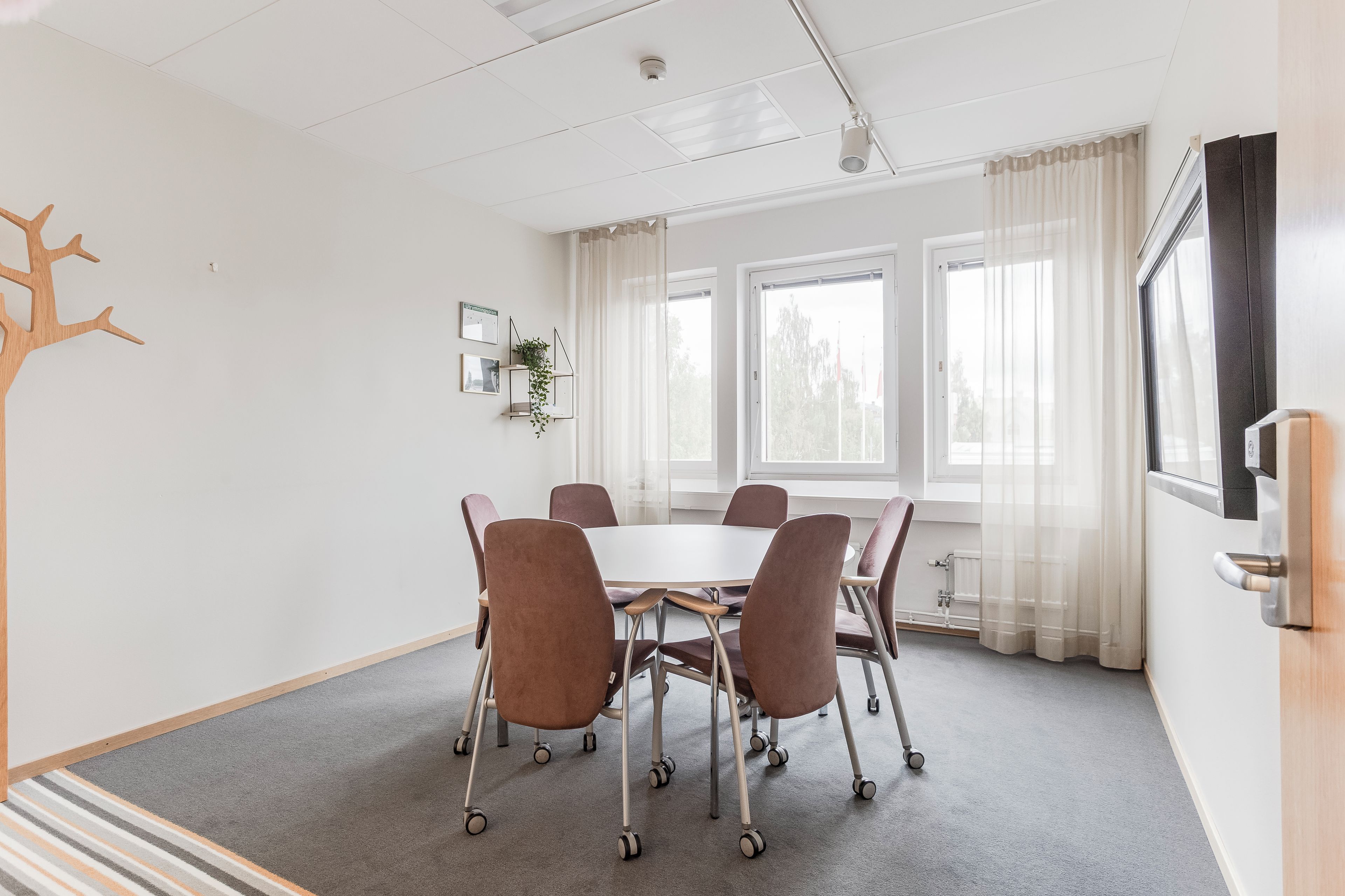 Un salón de conferencias con una mesa blanca, seis sillas y un ventanal con cortinas.