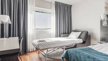 A hotel room with a bed, bedside table, lamp, and a view of the outdoors.