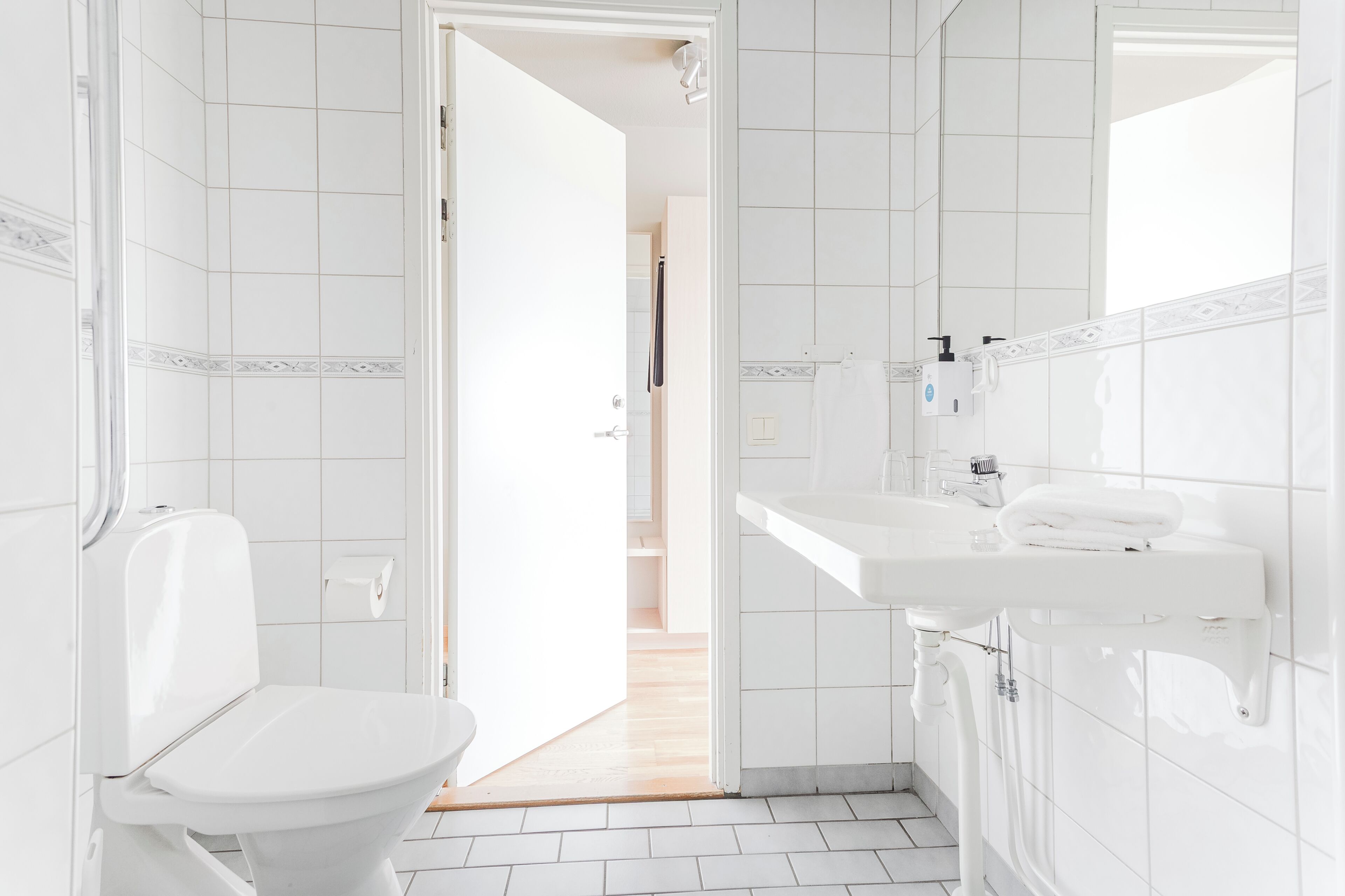 Une salle de bain avec des carreaux blancs, des toilettes, un lavabo et un miroir.