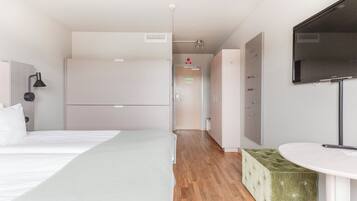 Ett modernt hotellrum med en säng, en grön pall, ett runt bord, en tv och en garderob.