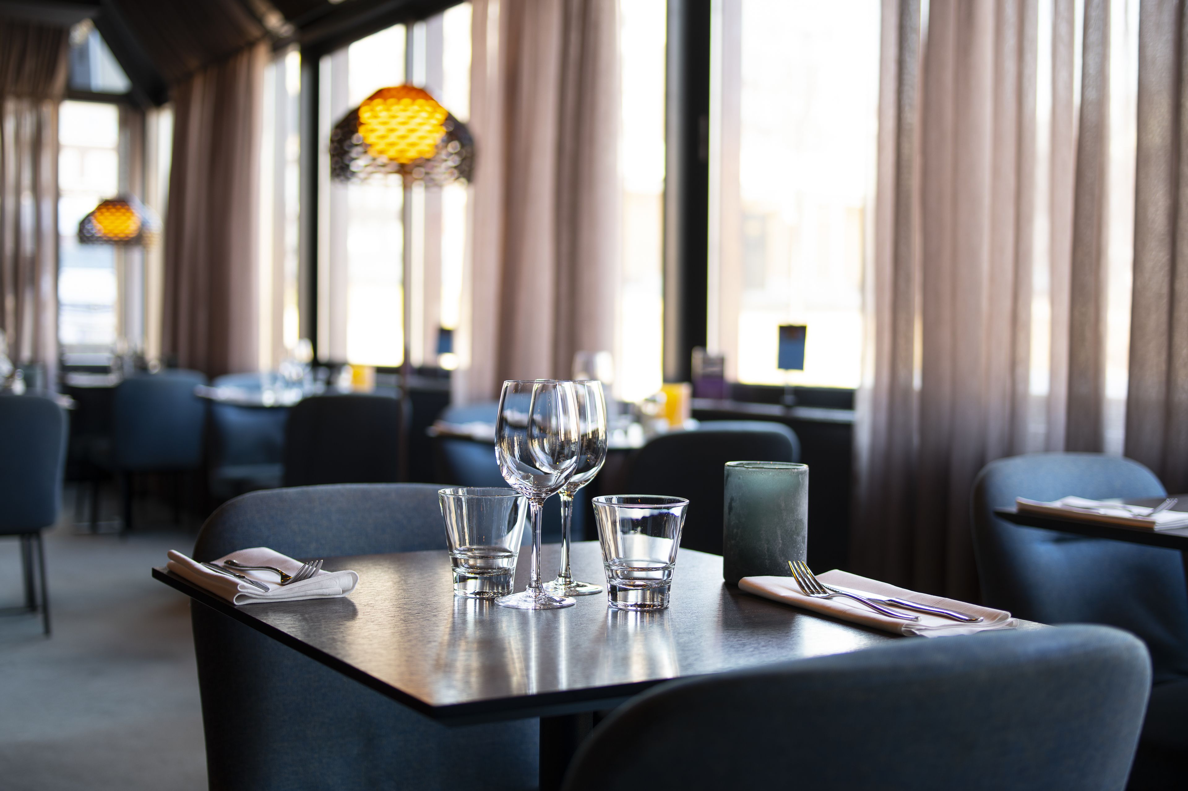 Ein Restaurantinnenraum mit gedeckten Tischen, darunter Weingläser und Besteck.