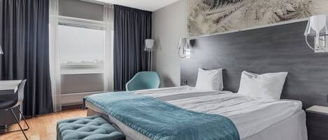 Una habitación de hotel moderna con una cama grande, un escritorio, una silla y vistas de la ciudad.
