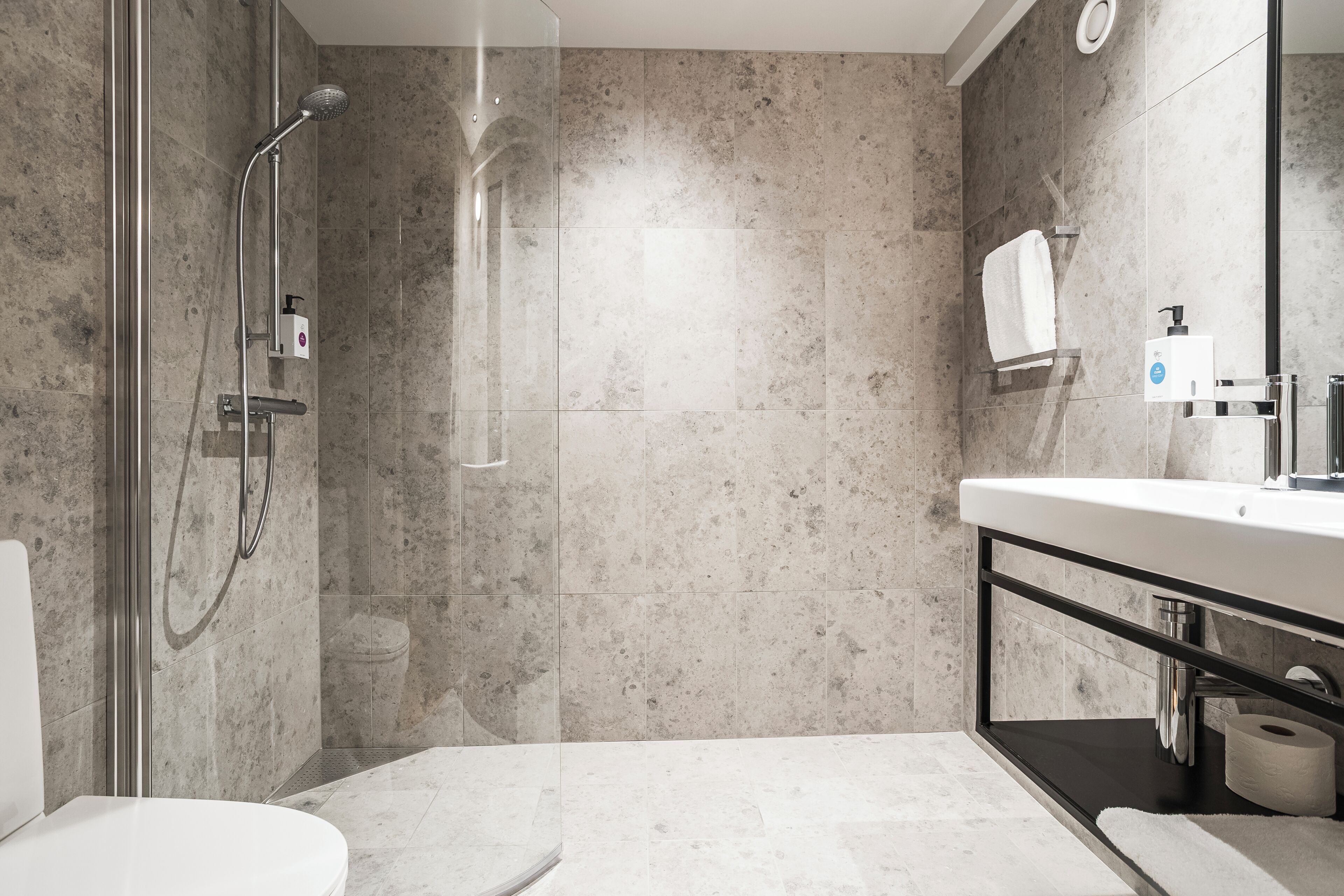 A modern bathroom with a glass-enclosed shower, a toilet, a sink with a mirror, and a towel rack.