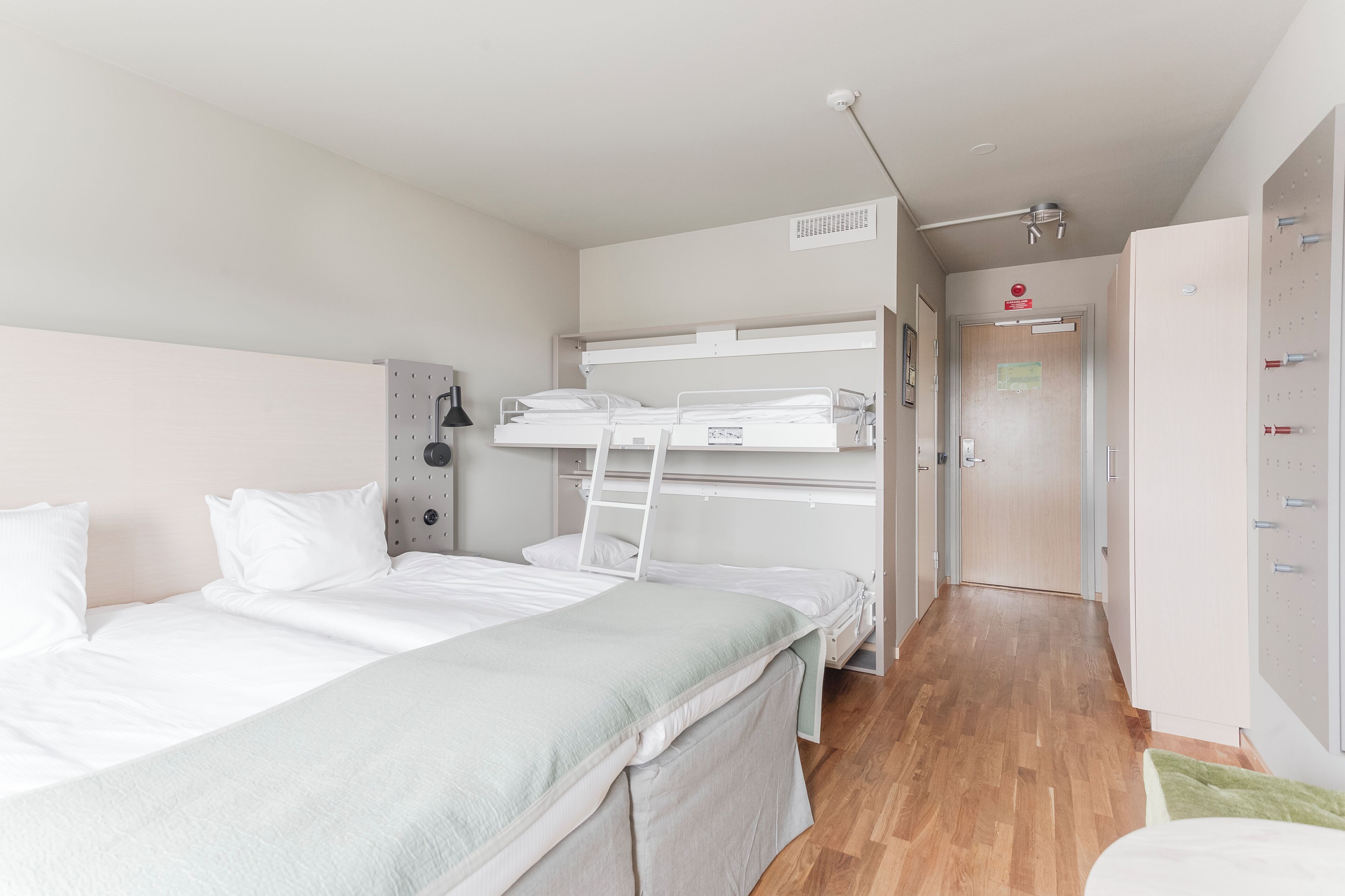 A bunk bed room with a wooden floor, a desk, and a wardrobe.