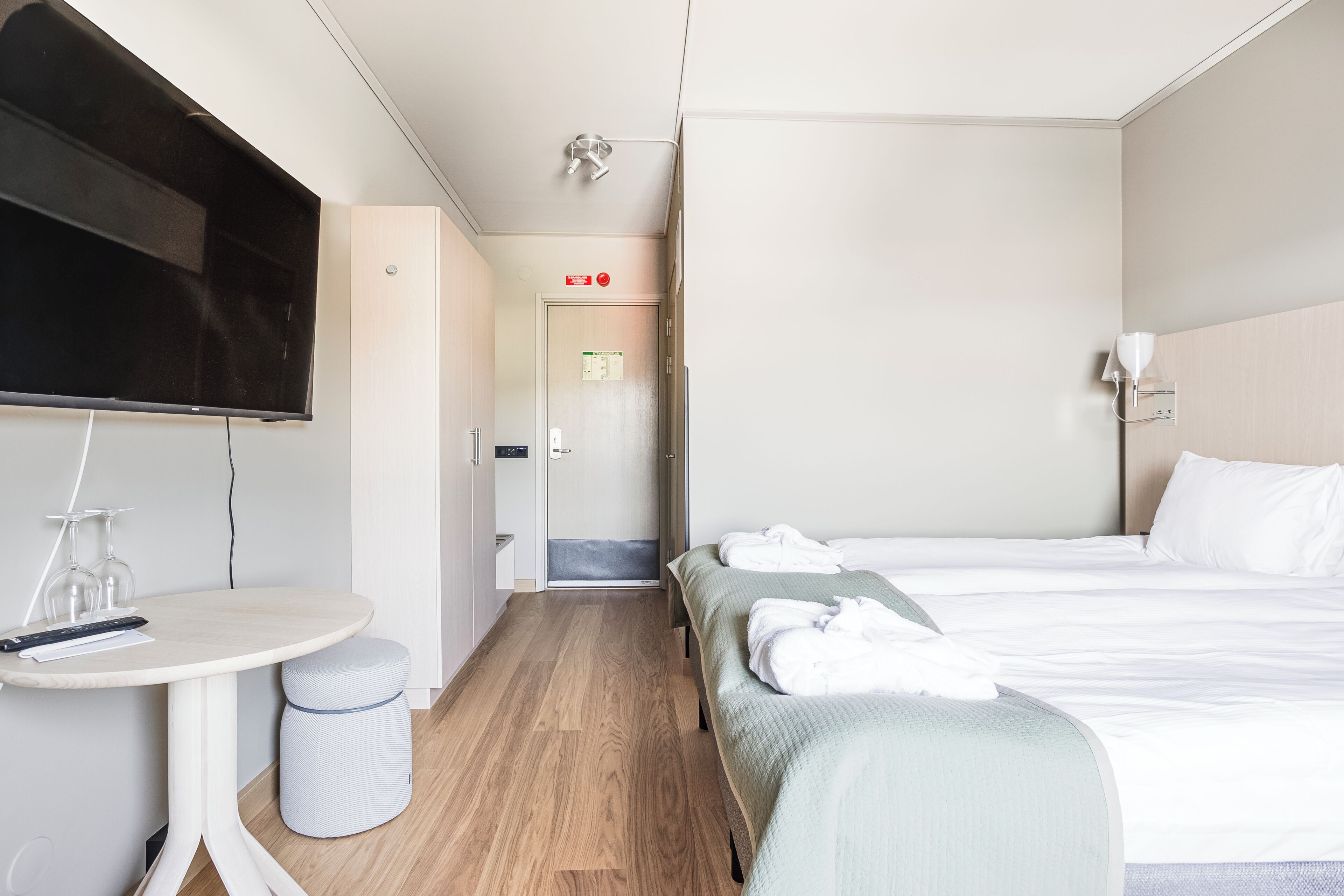 Een hotelkamer met een bed, nachtkastje, televisie en een klein zithoekje.