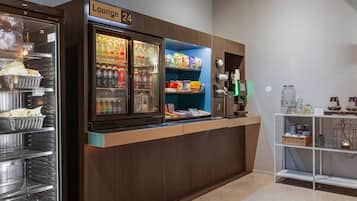 A lounge area with a refrigerator stocked with beverages, snack shelves, and a coffee machine.