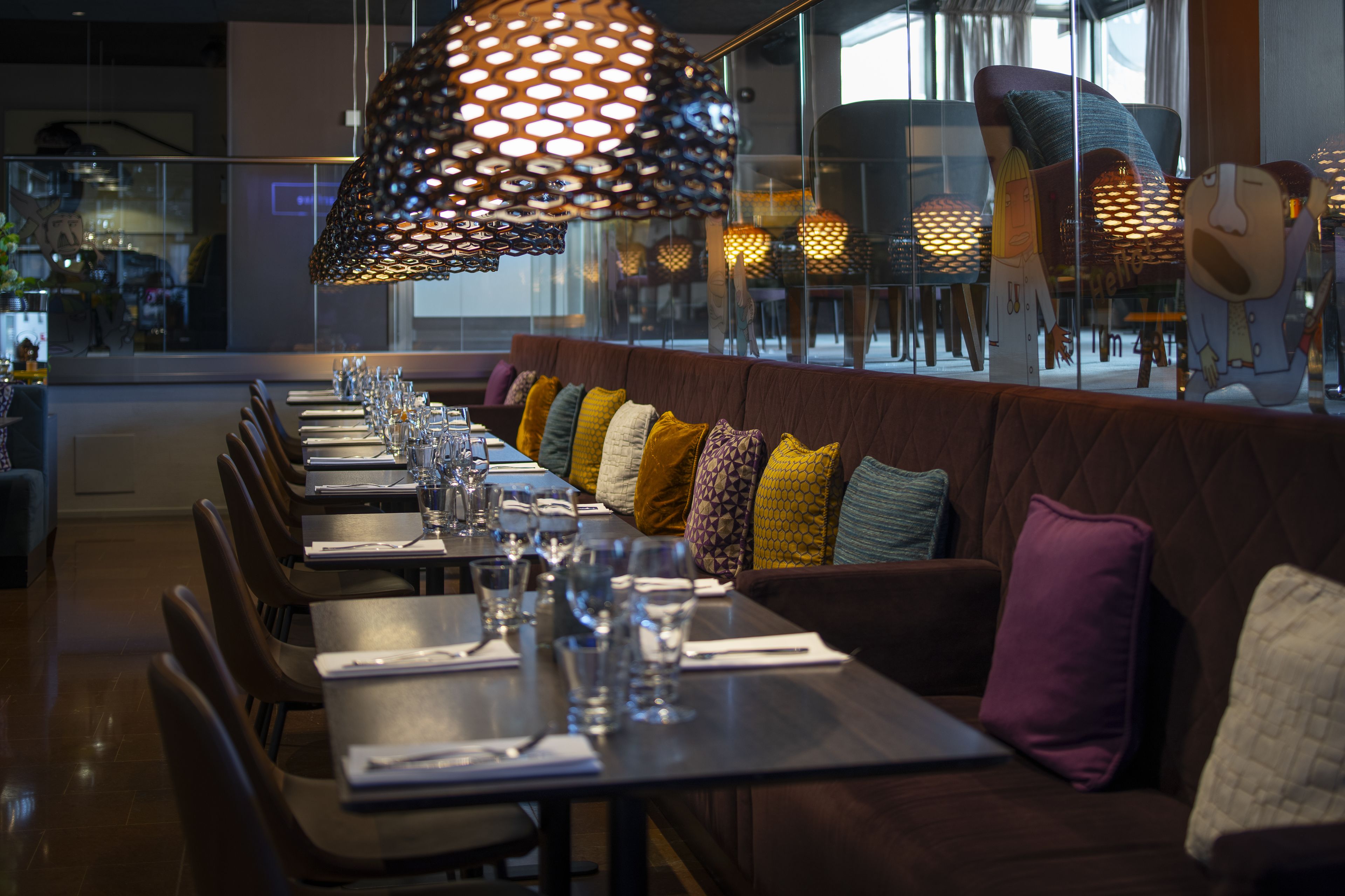 Un restaurante con una mesa larga dispuesta para comer, asientos acolchados y lámparas decorativas colgantes.