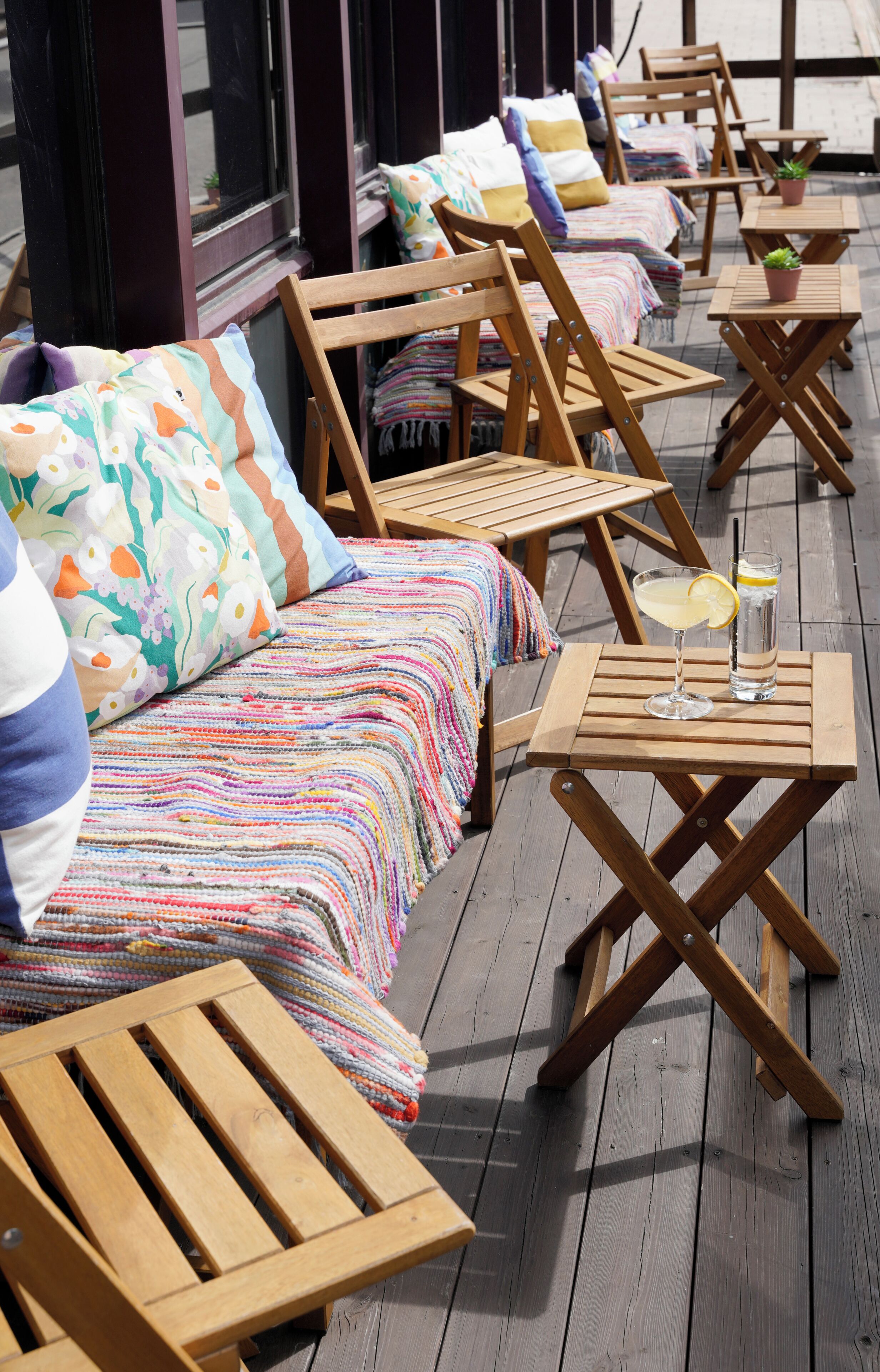 A deck with wooden lounge chairs, a sofa with colorful bedding, and a table with a drink.