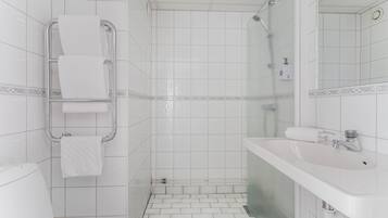 Une salle de bain avec des carreaux blancs, une douche en verre, un lavabo blanc et un porte-serviettes.