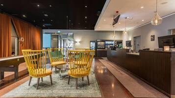 Eine Hotelhalle mit Rezeption, einer Sitzecke mit Stühlen und einer Kaffeemaschine.