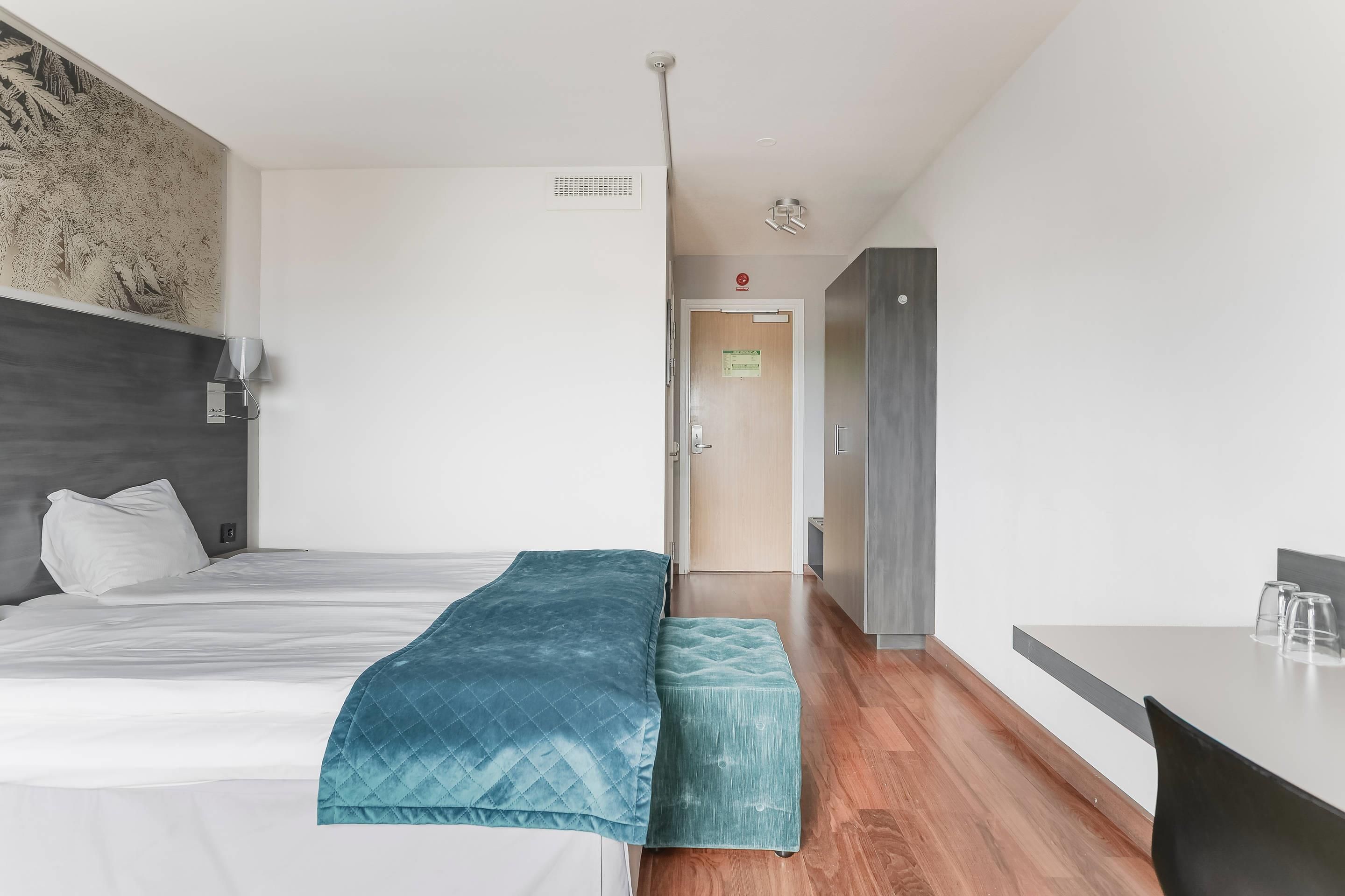 Quarto de hotel com cama, um banco, escrivaninha e guarda-roupa.