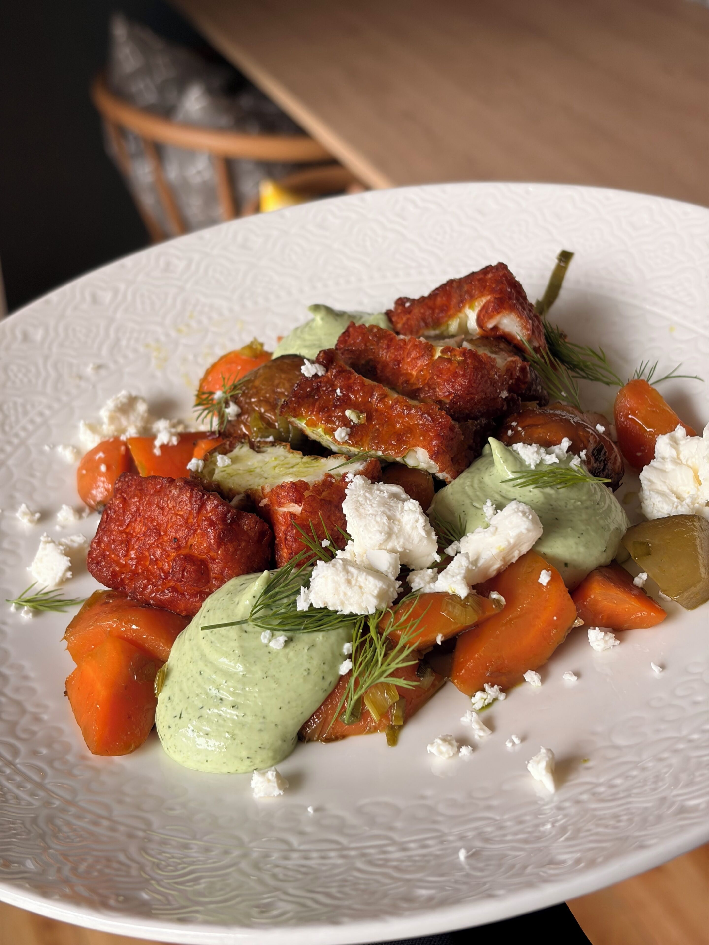 A white plate with a salad containing carrots, a green sauce, and crumbled cheese.