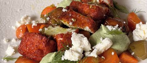 A white plate with a salad containing carrots, a green sauce, and crumbled cheese.